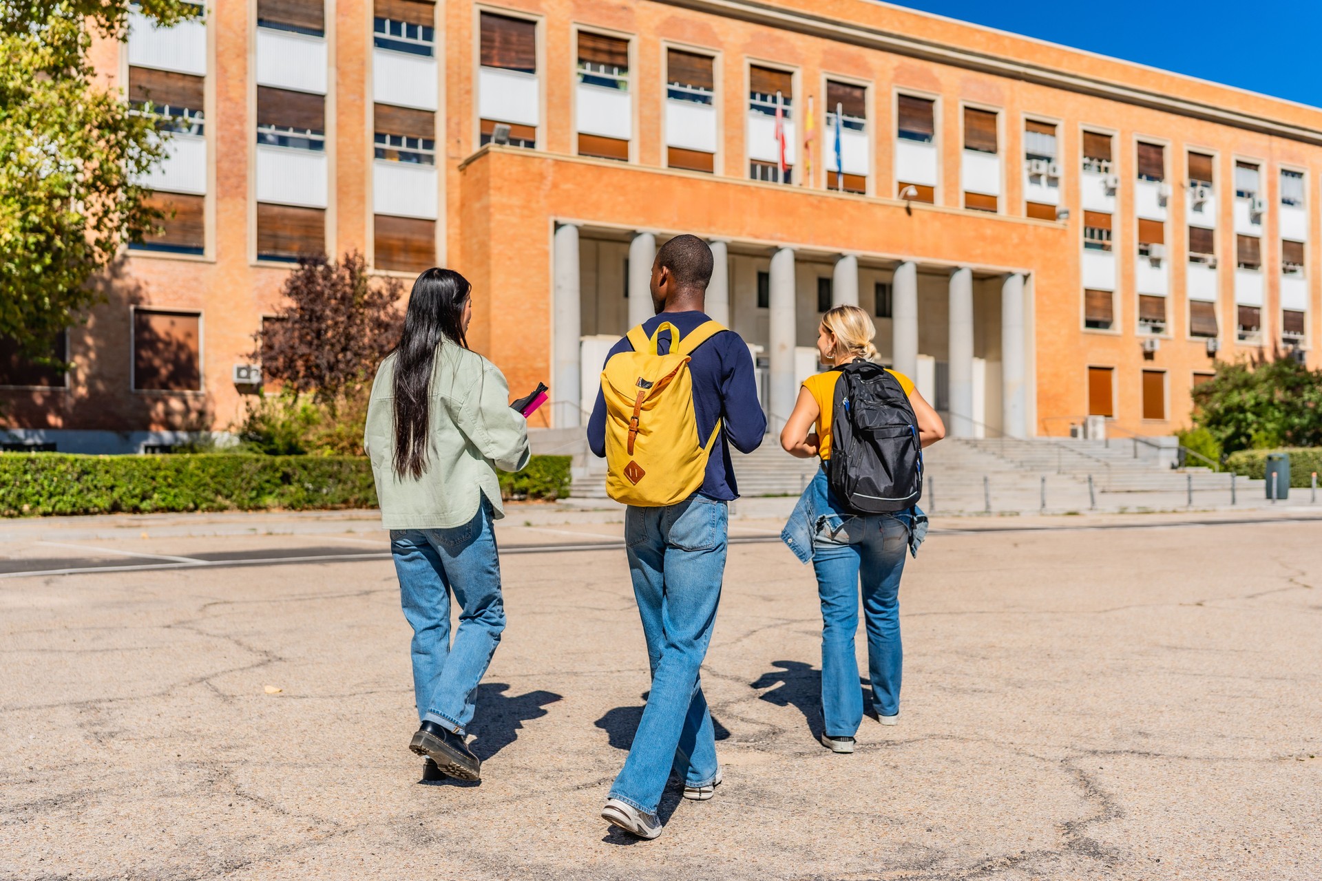 Three students walking along the campus in a sunny day