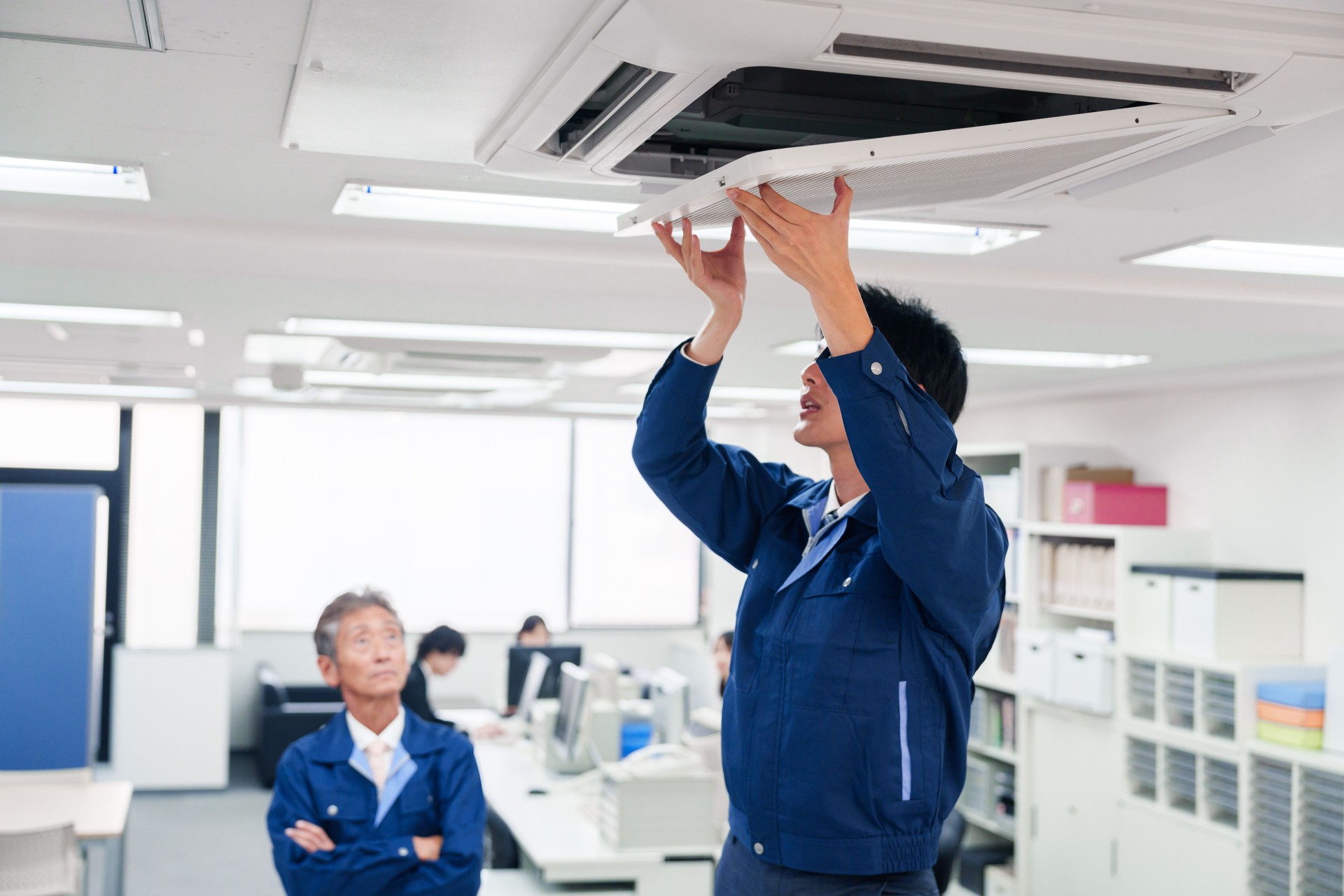 Man in work clothes inspecting a building's air conditioner